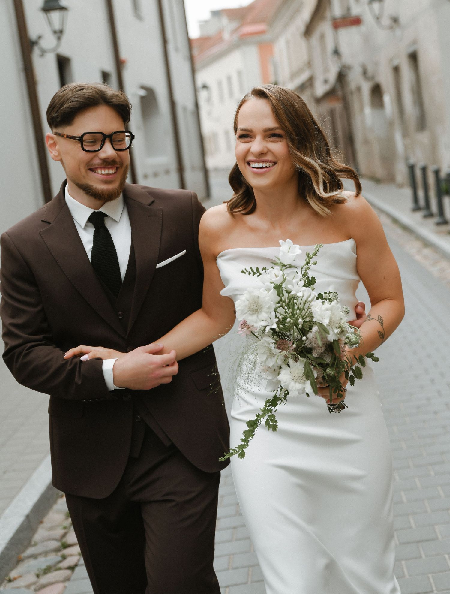 A couple shares romantic moments on a cobblestone street with the bride holding a delicate white and green bouquet.