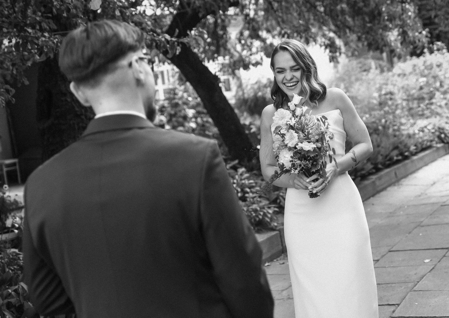 A black and white wedding photo capturing a romantic first look moment in a garden setting with a beautiful bouquet.