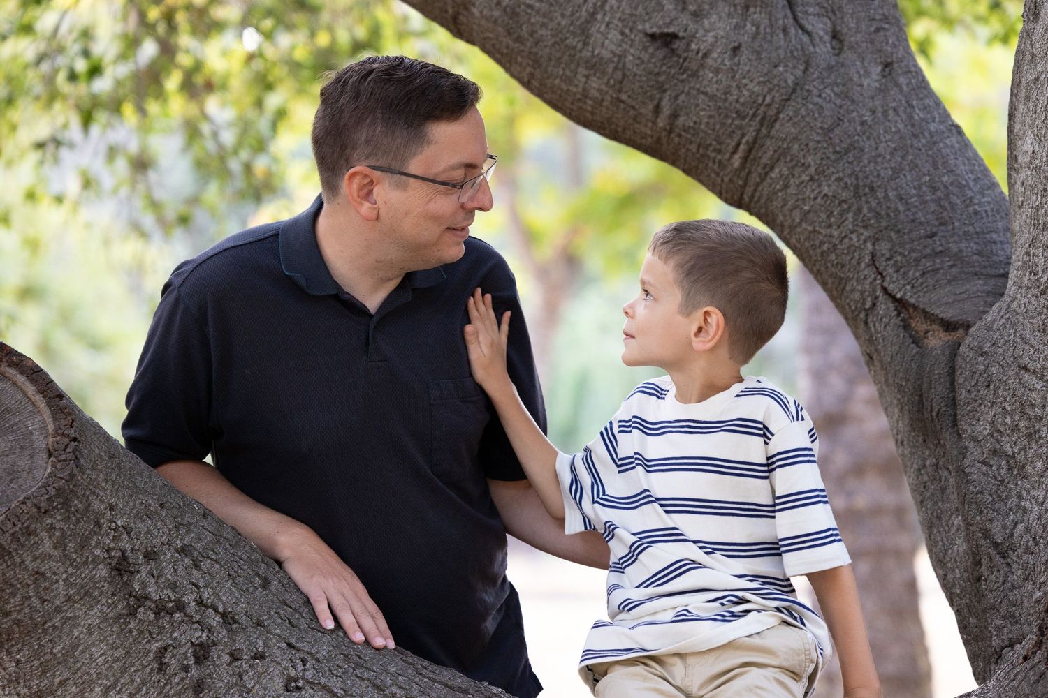 A dad and his son interact playfully near a tree trunk in the Bay Area.