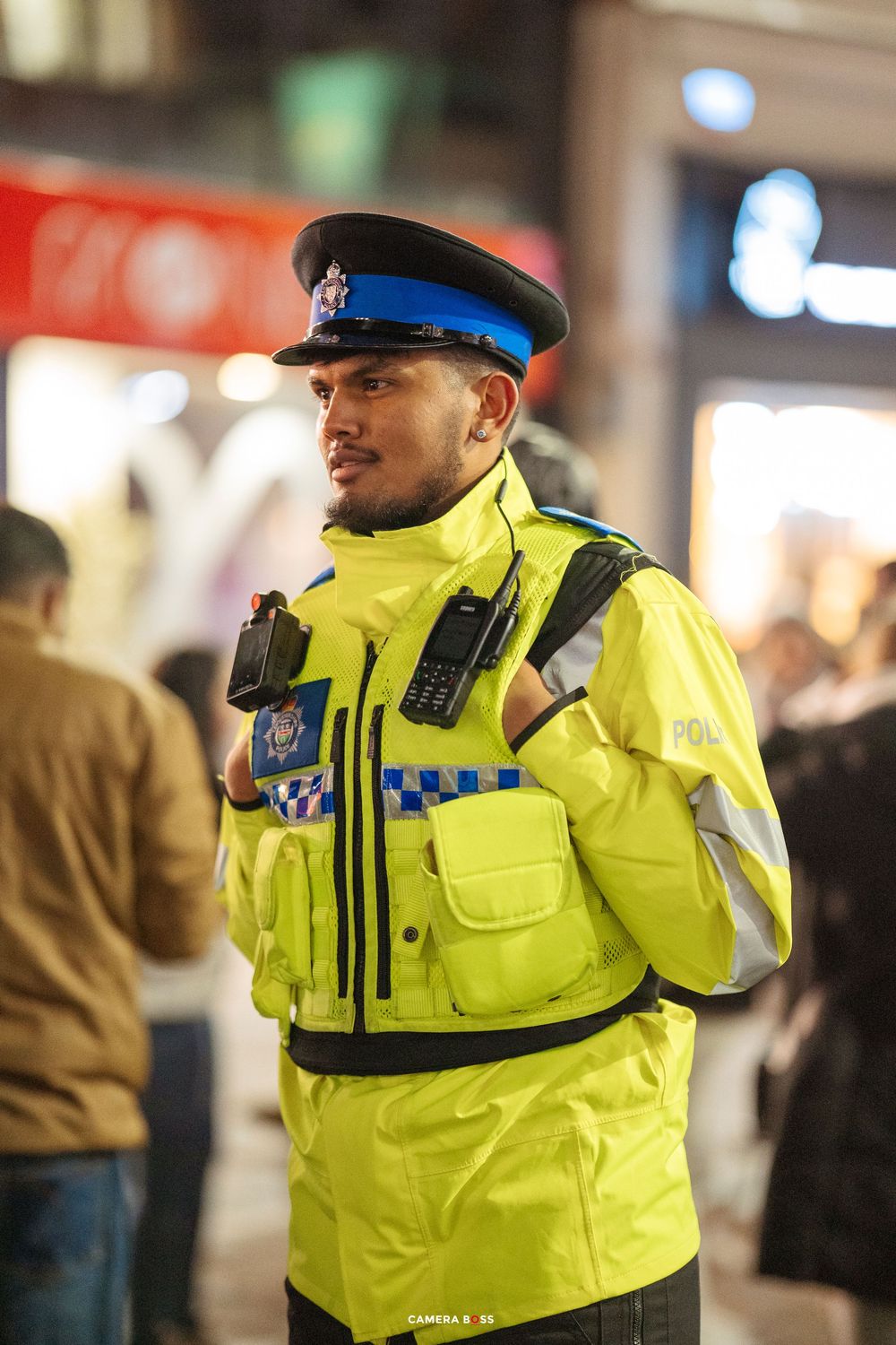 Police officer in high-visibility yellow jacket stands on duty during nighttime patrol.