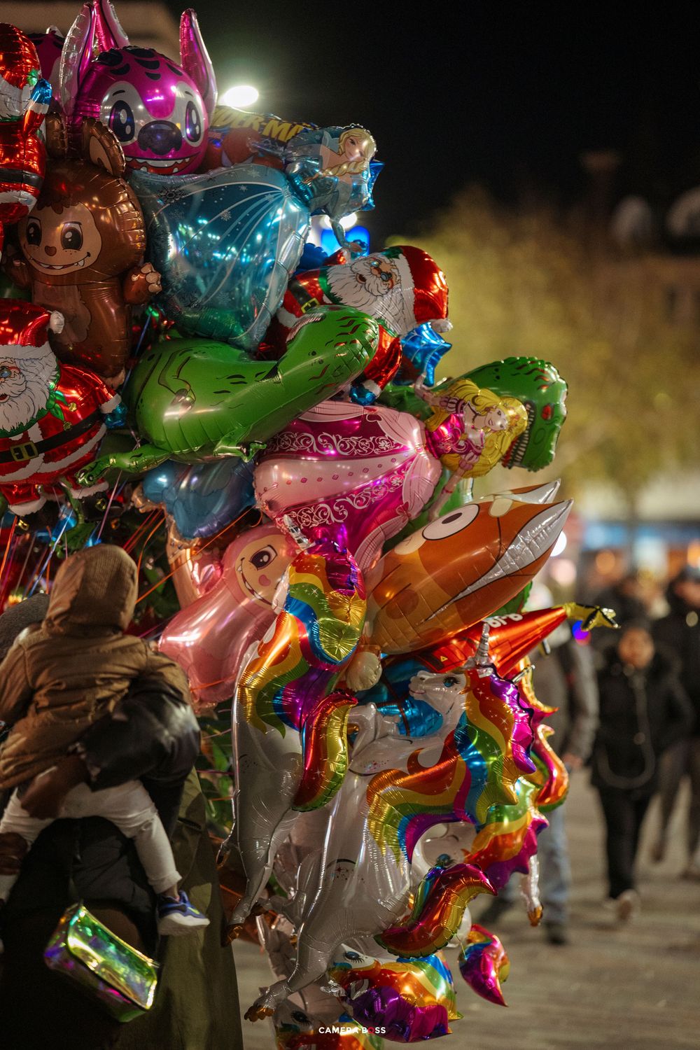 Colorful helium balloons in various shapes and characters float together against a dark nighttime background.