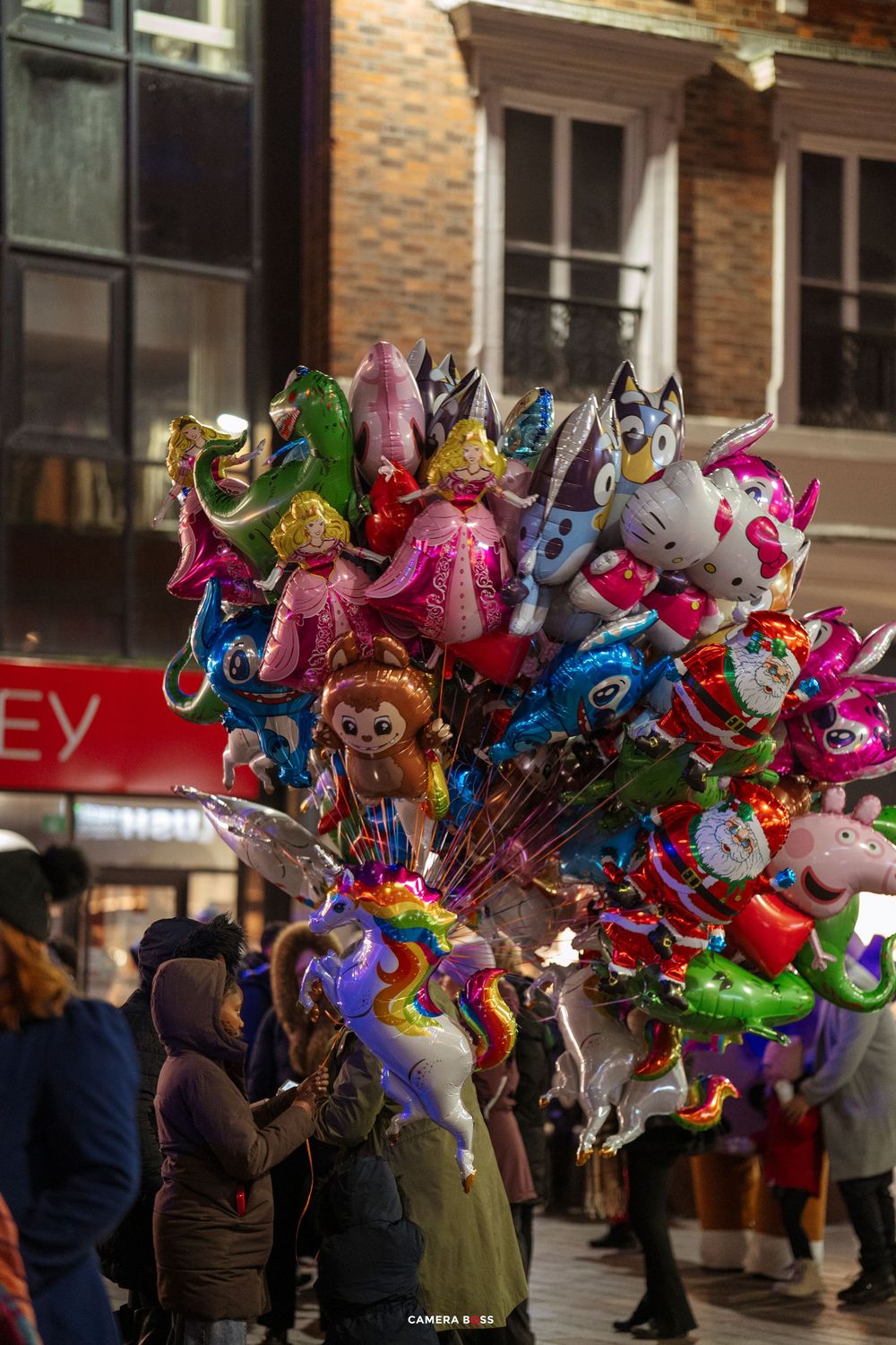 Colorful character balloons and inflatables being sold by vendors on a city street during a festive event.