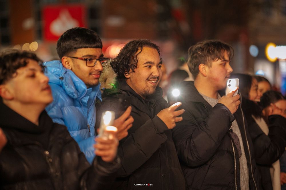 Crowd of people holding up illuminated phones at a nighttime gathering or event.