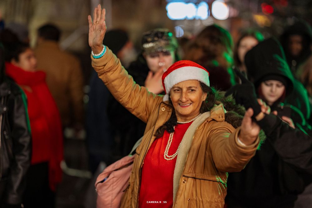 People waving and celebrating at a festive nighttime event with colorful lights in the background.