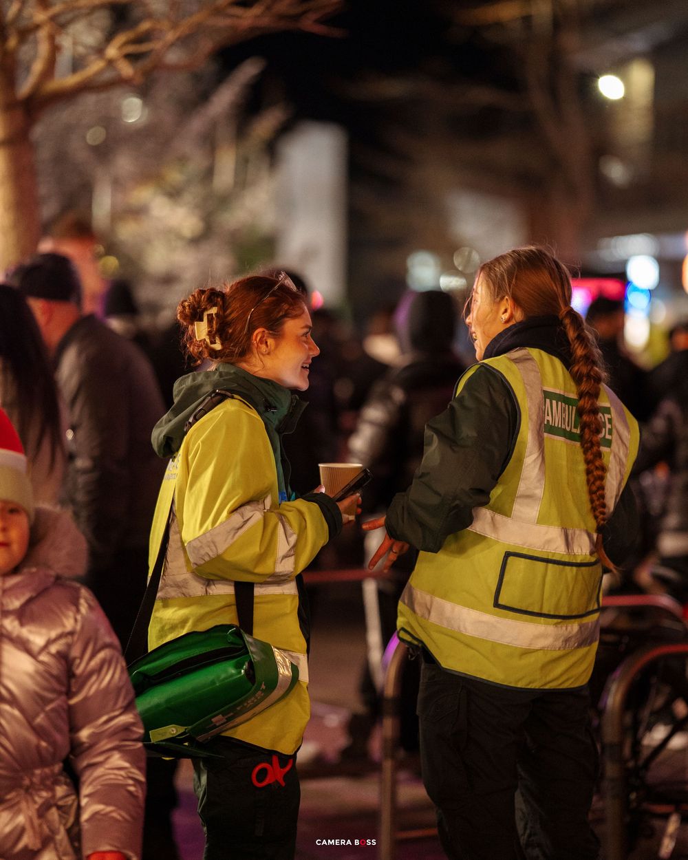 Security personnel in high-visibility yellow vests patrol a crowded nighttime street event.