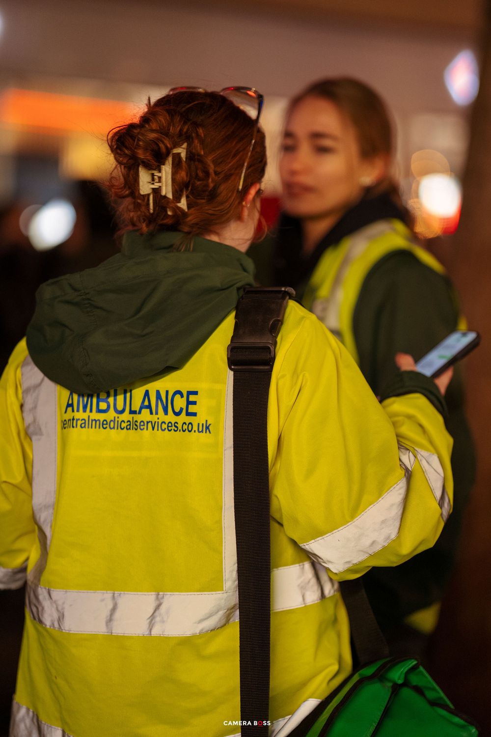 Emergency medical personnel in high-visibility yellow vests stand together at night.