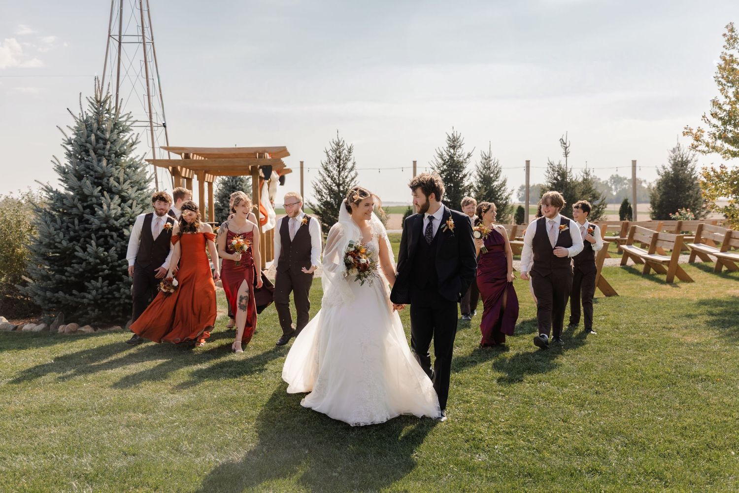 Wedding party poses together outdoors with scenic mountain backdrop and rustic wooden arch.