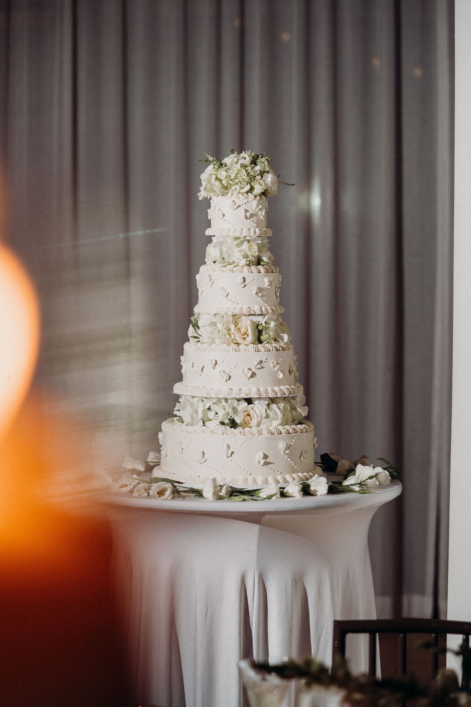 Elegant white tiered wedding cake with floral decorations displayed on round table at reception venue.