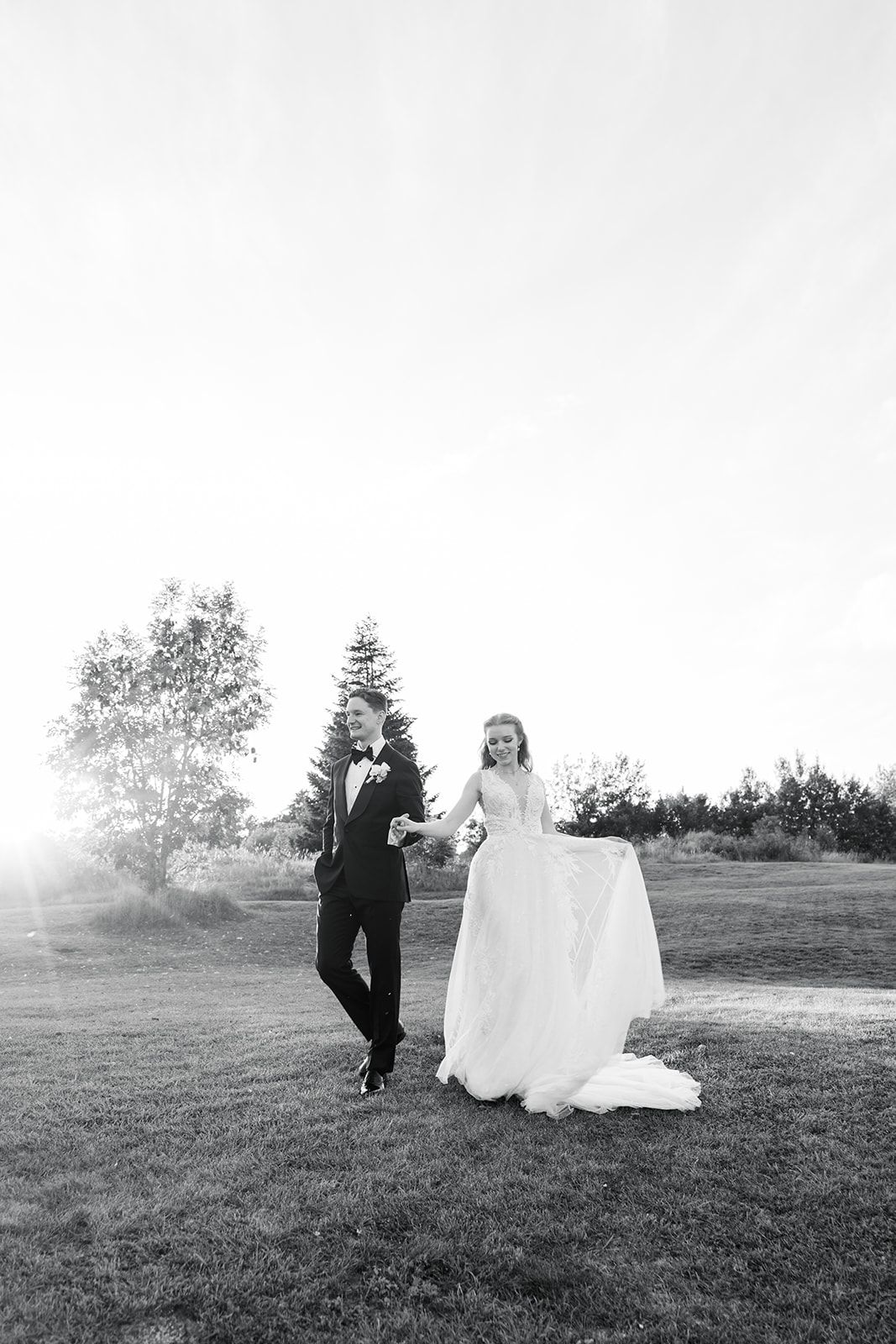 A romantic black and white wedding photo series showing a couple walking together across a grassy hillside.