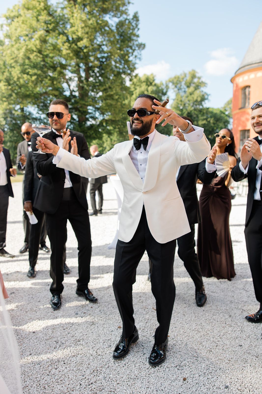 Groomsmen in black and white tuxedos perform synchronized dance moves at outdoor wedding celebration.