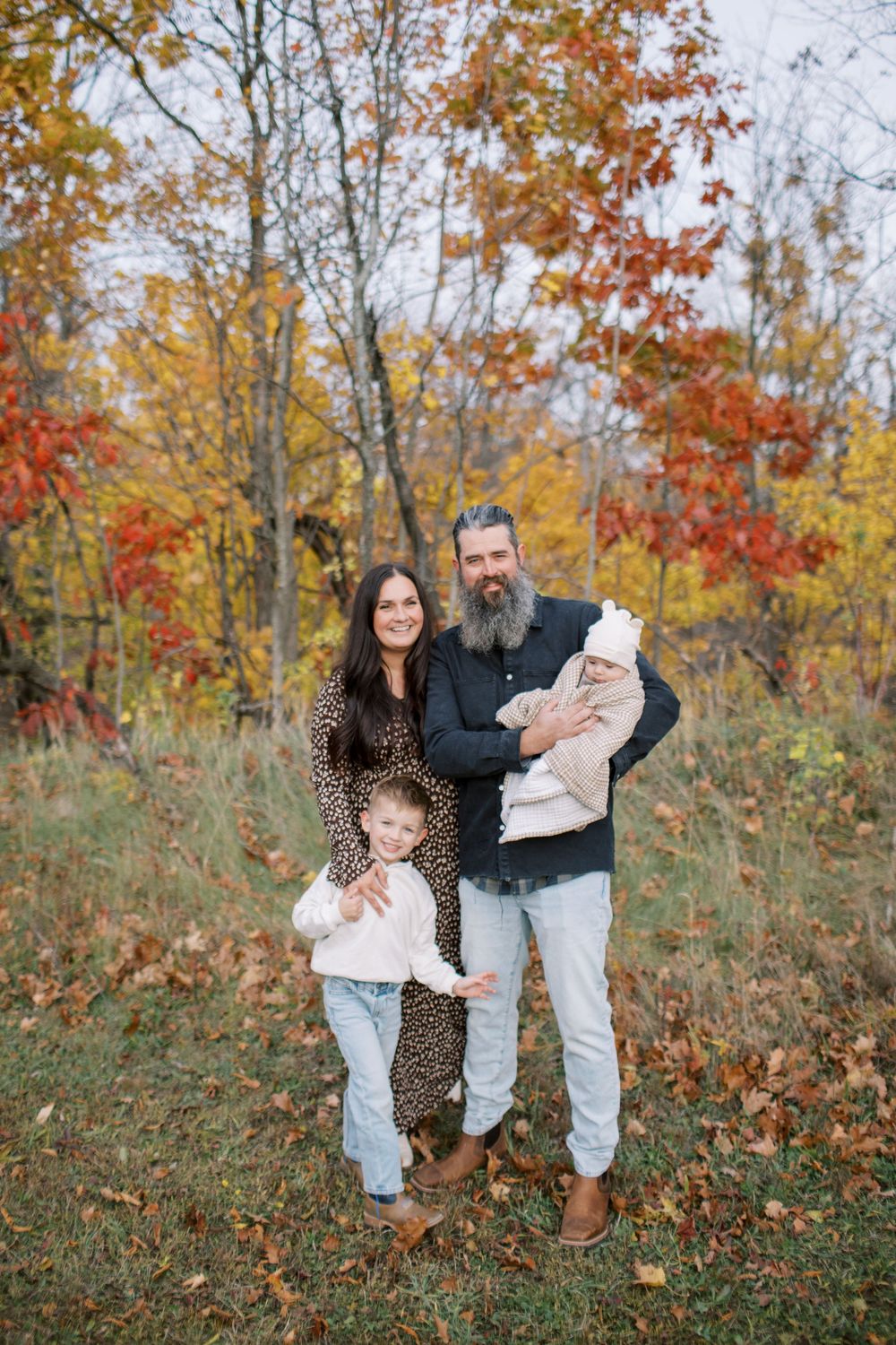 A playful family photoshoot in an autumn forest setting with colorful fall foliage in the background.