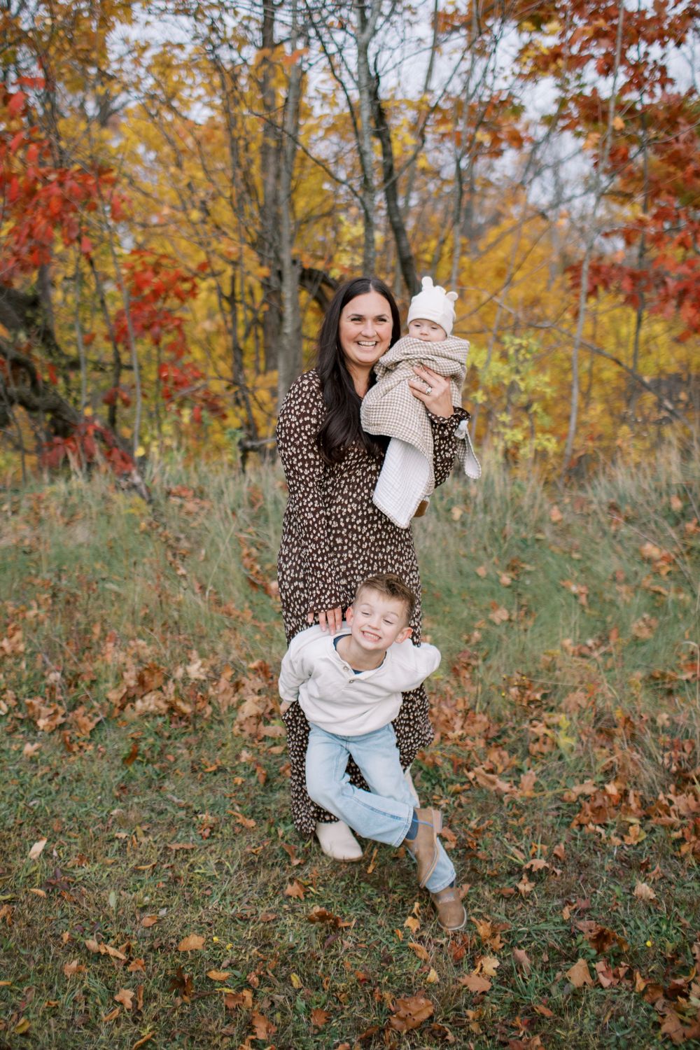 Candid family moment captured against vibrant autumn trees with fallen leaves scattered on the ground.