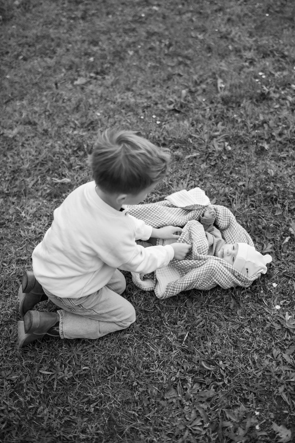 A series of black and white photographs showing a small child lying in grass with a doll or toy in a gentle sequence.