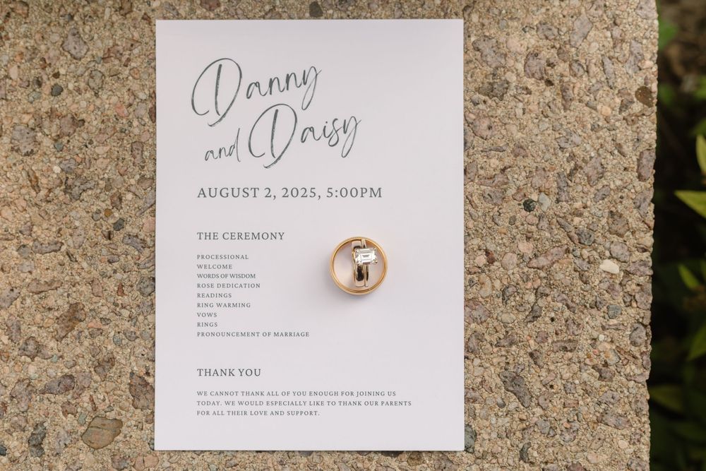 Wedding invitation and ring details photographed on a textured stone surface with natural lighting.