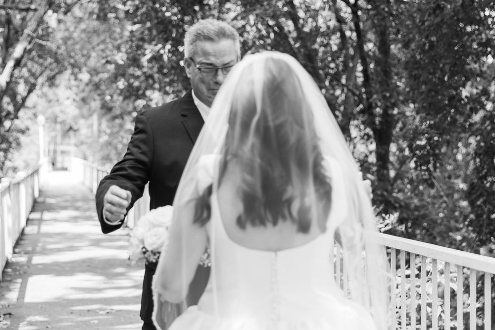 A wedding couple walks down a tree-lined path while holding hands and sharing a romantic moment together.