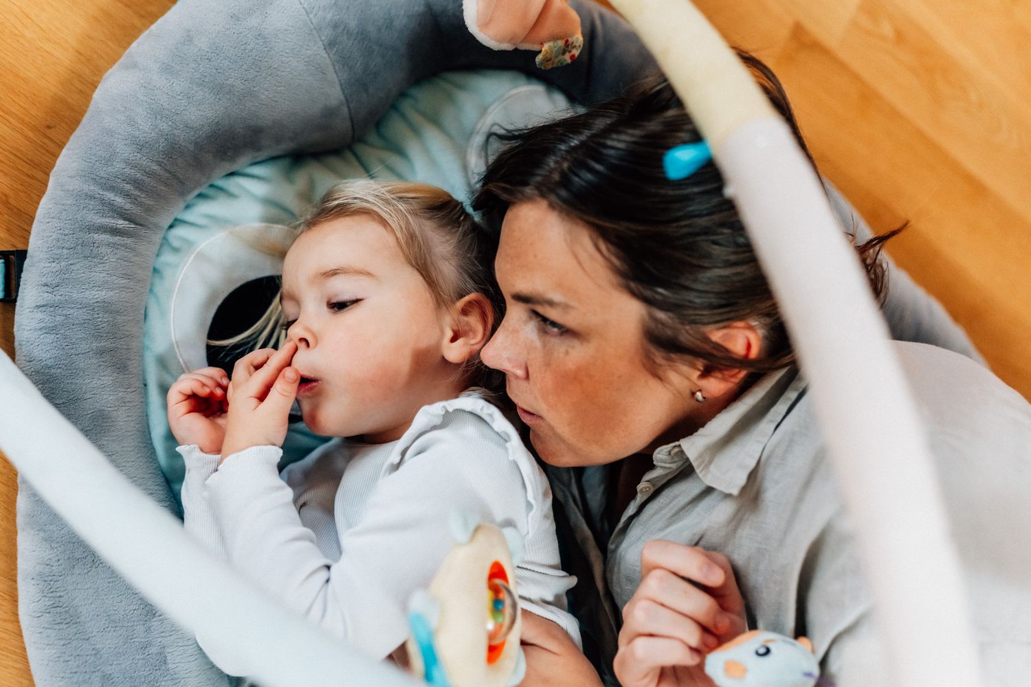 Ett barn ligger på golvet på en filt och petar i näsan och hennes mamma ligger bredvid.