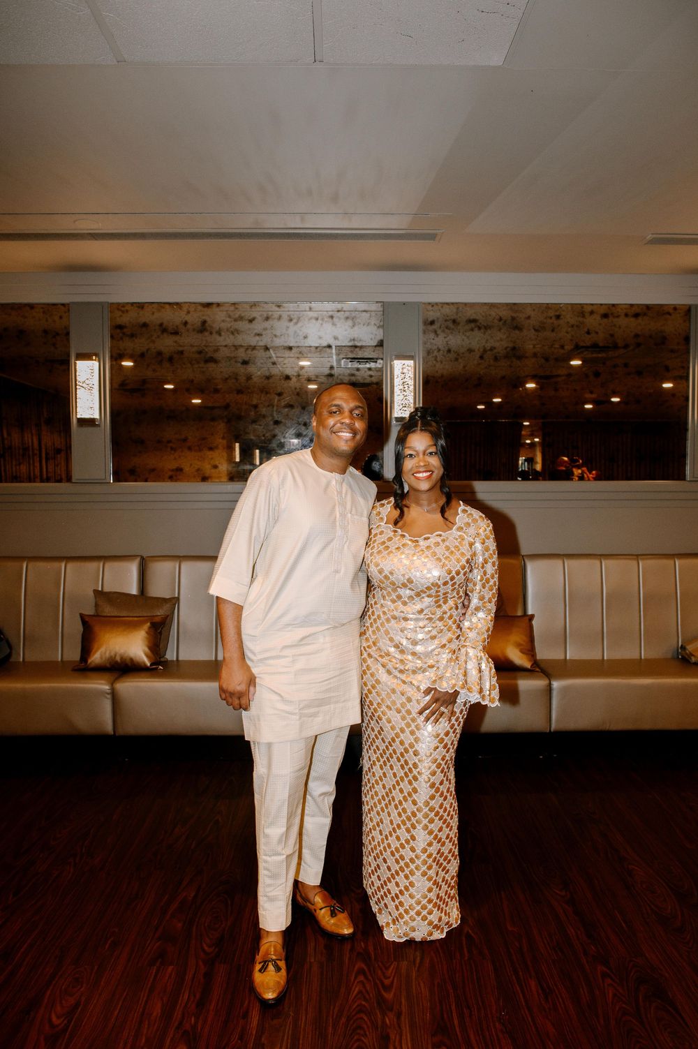 Two people in white and sparkly gold outfits dance together on a wooden floor in a warmly lit indoor venue.