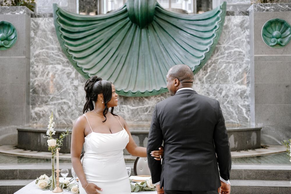 Wedding couple posing against a decorative green and white architectural backdrop.