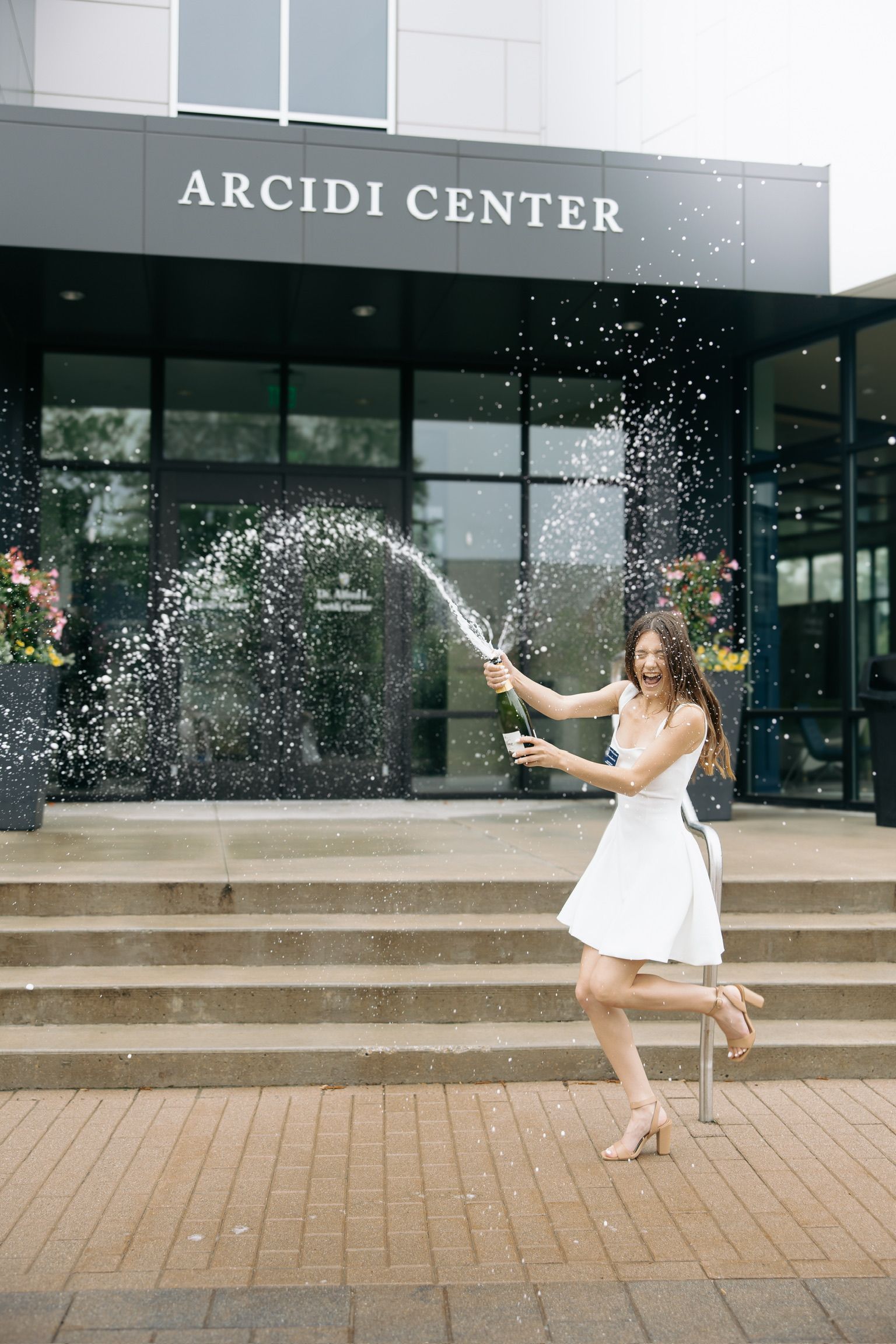 Person in white dress throwing confetti outside Arcidi Center building.