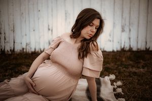 Woman in a flowing beige dress poses gracefully on the ground during a dreamy outdoor photo session.