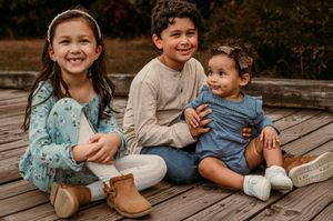 Three children sitting together on a wooden deck wearing casual clothing and boots in Stafford VA.
