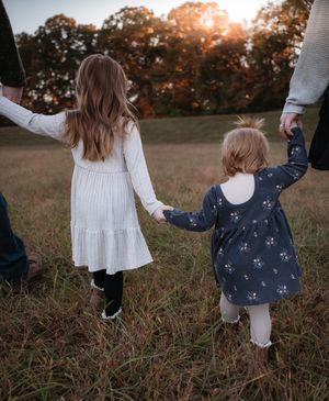 Two children holding hands with parents while walking in a field at sunset in Stafford VA.