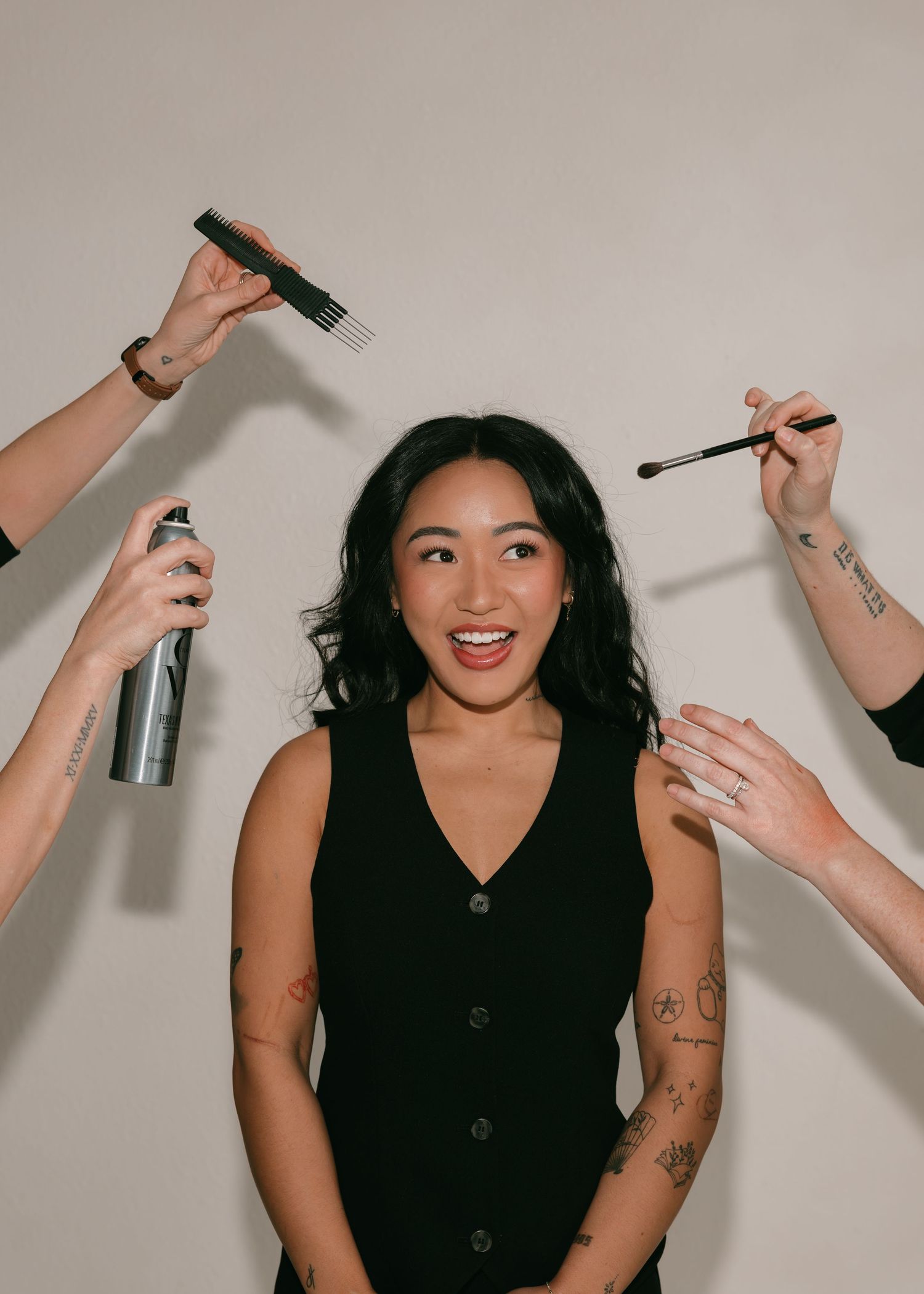 A group of people in black attire sit on chairs while getting their makeup professionally done in a bright studio space.