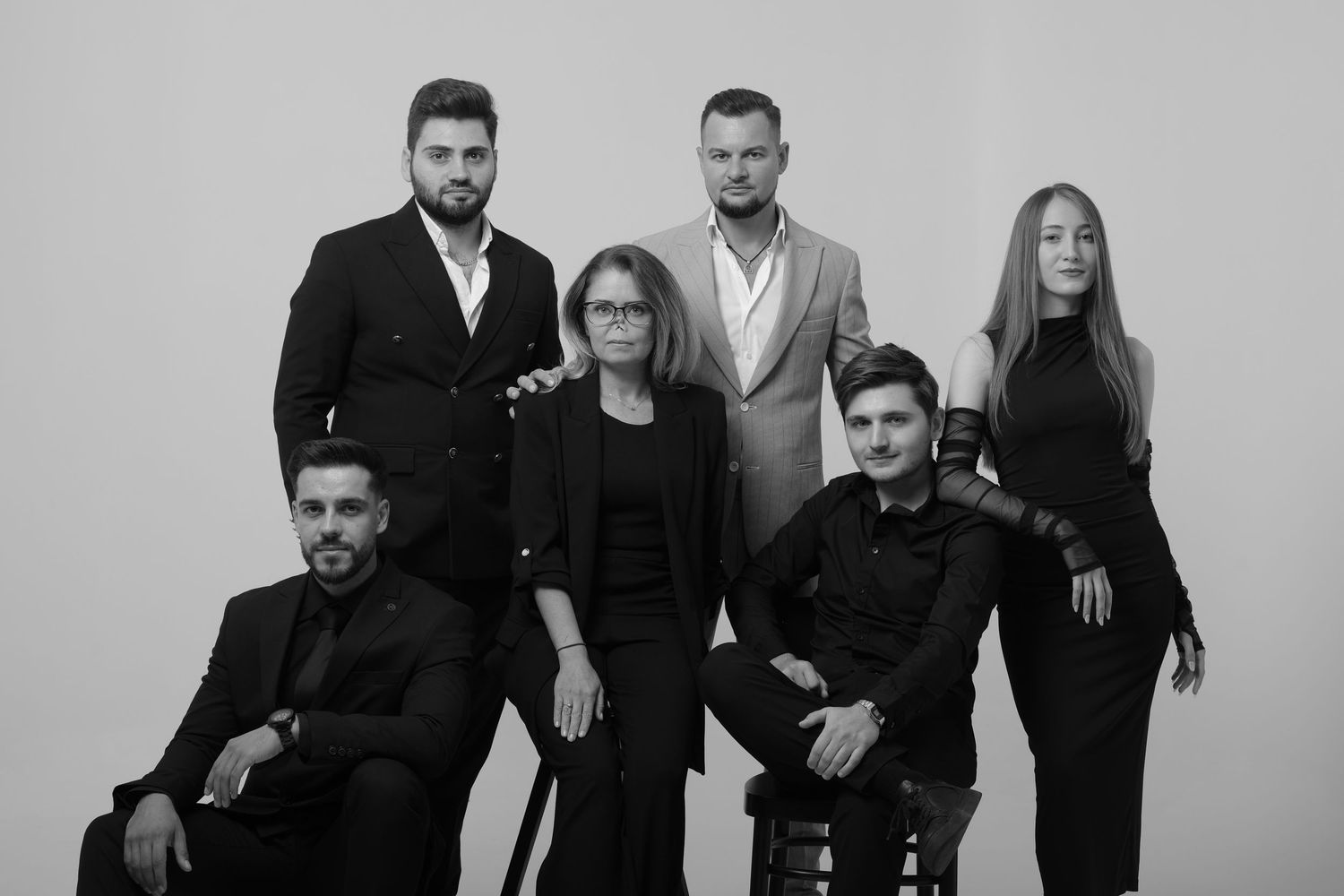 A group of performers pose together in formal black and white attire for a professional photoshoot.