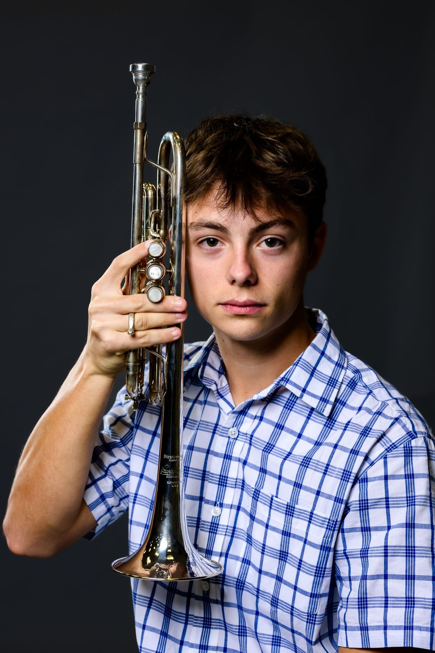 Person in blue checkered shirt holding up a trumpet in various poses against dark background.
