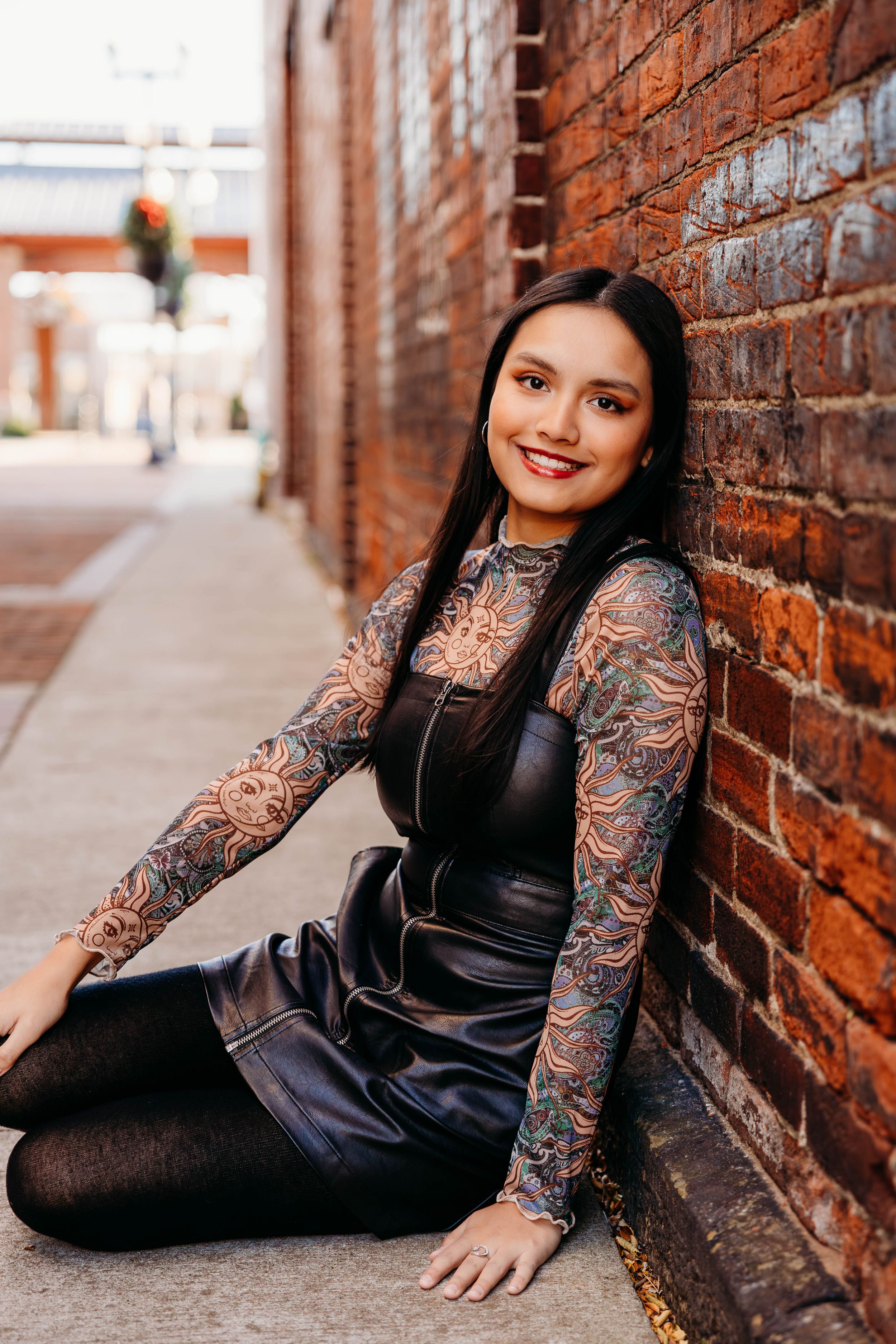 Person in black outfit with lace sleeves poses against rustic brick wall in urban setting.