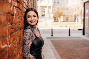 Professional portrait session with black lace dress against rustic brick wall background in urban setting.