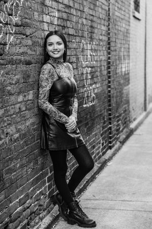 Black and white portrait series showing casual poses against industrial brick wall background.