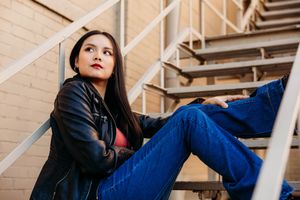 A person in blue jeans and dark top reclines on white metal stairs in an urban environment.