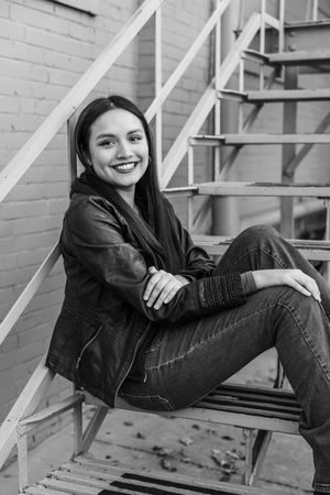 A person in black casual attire relaxes on wooden stairs against a white brick wall in a series of candid poses.