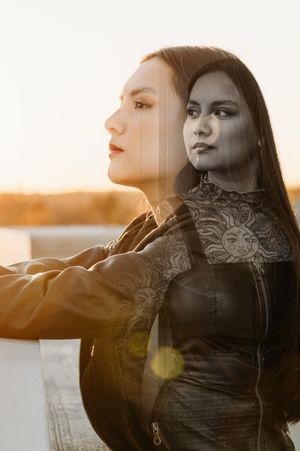 Silhouette of a woman with long dark hair gazing at sunset with sun flare creating a dreamy atmospheric effect.