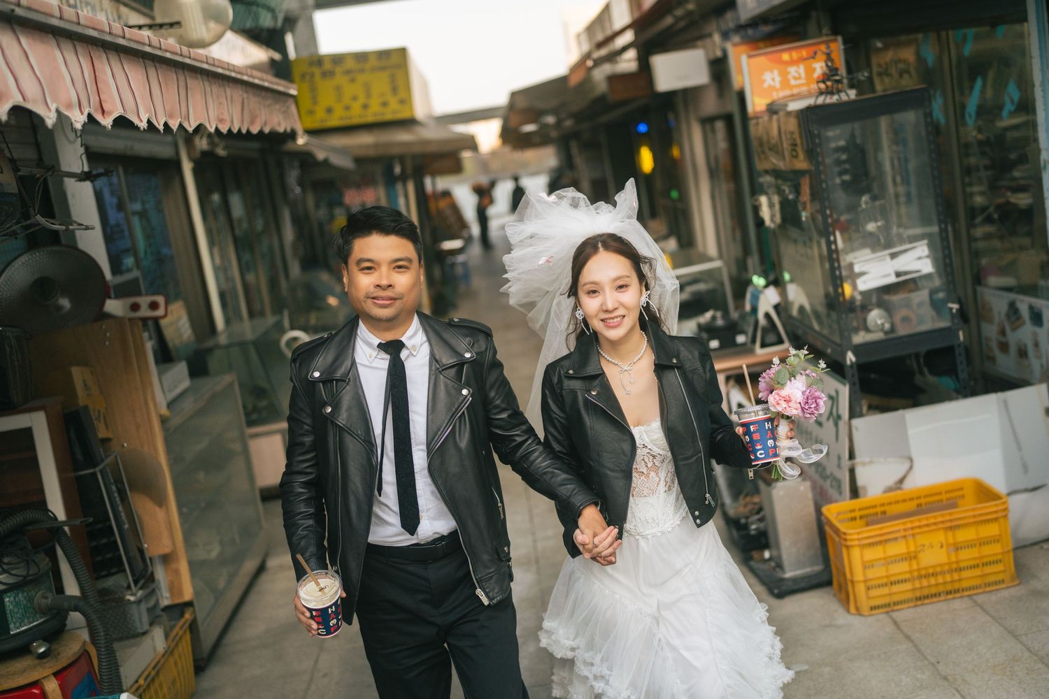 Newlywed couple walking through a traditional Asian market alley in formal wedding attire.