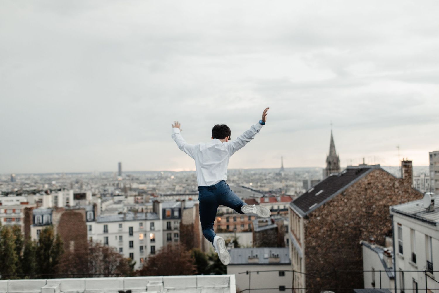 Bar mitzvah sautant en l’air face aux toits de Paris, photo dynamique et joyeuse en hauteur.