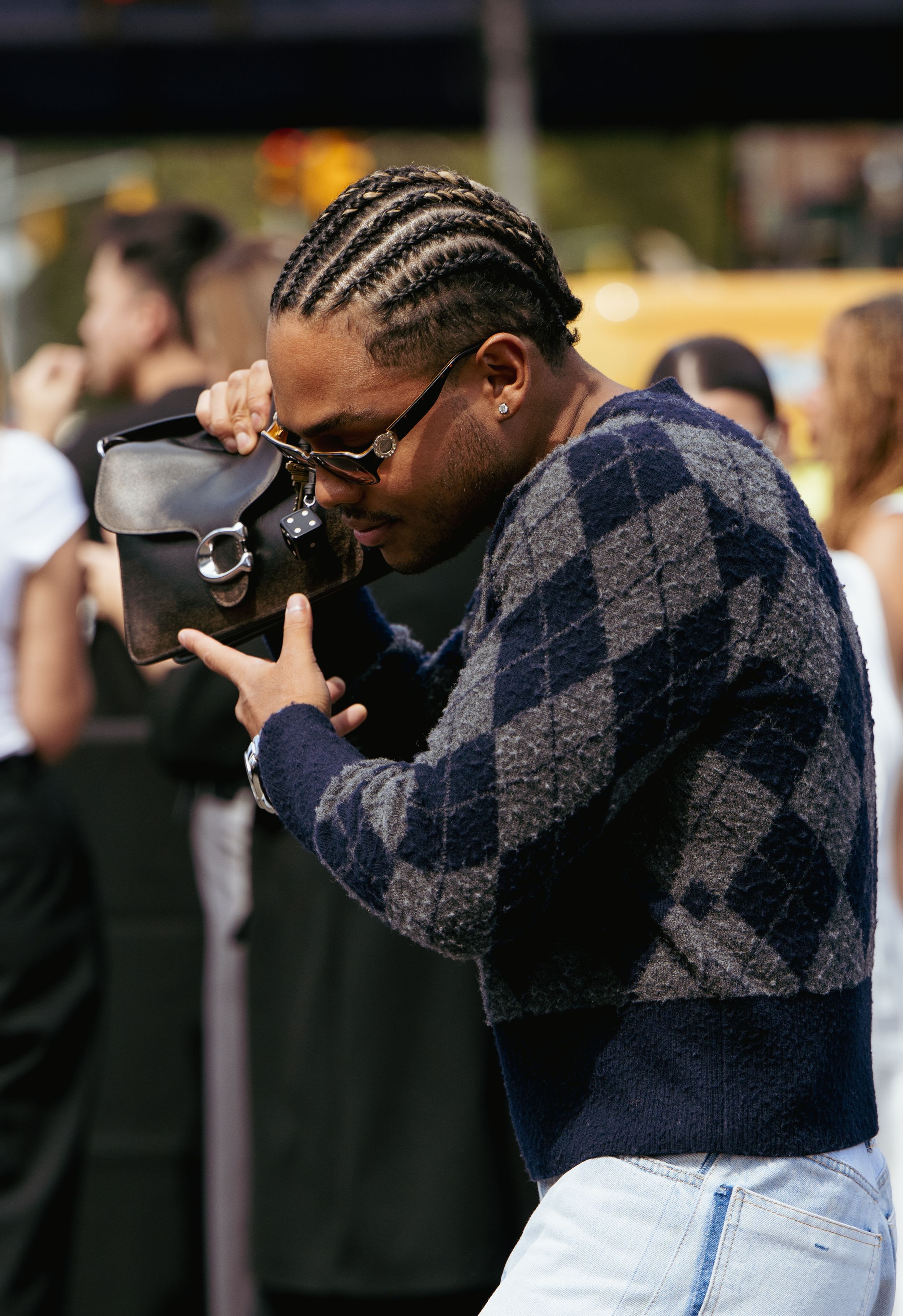 A person in a dark sweater and light pants looks down while walking outdoors.