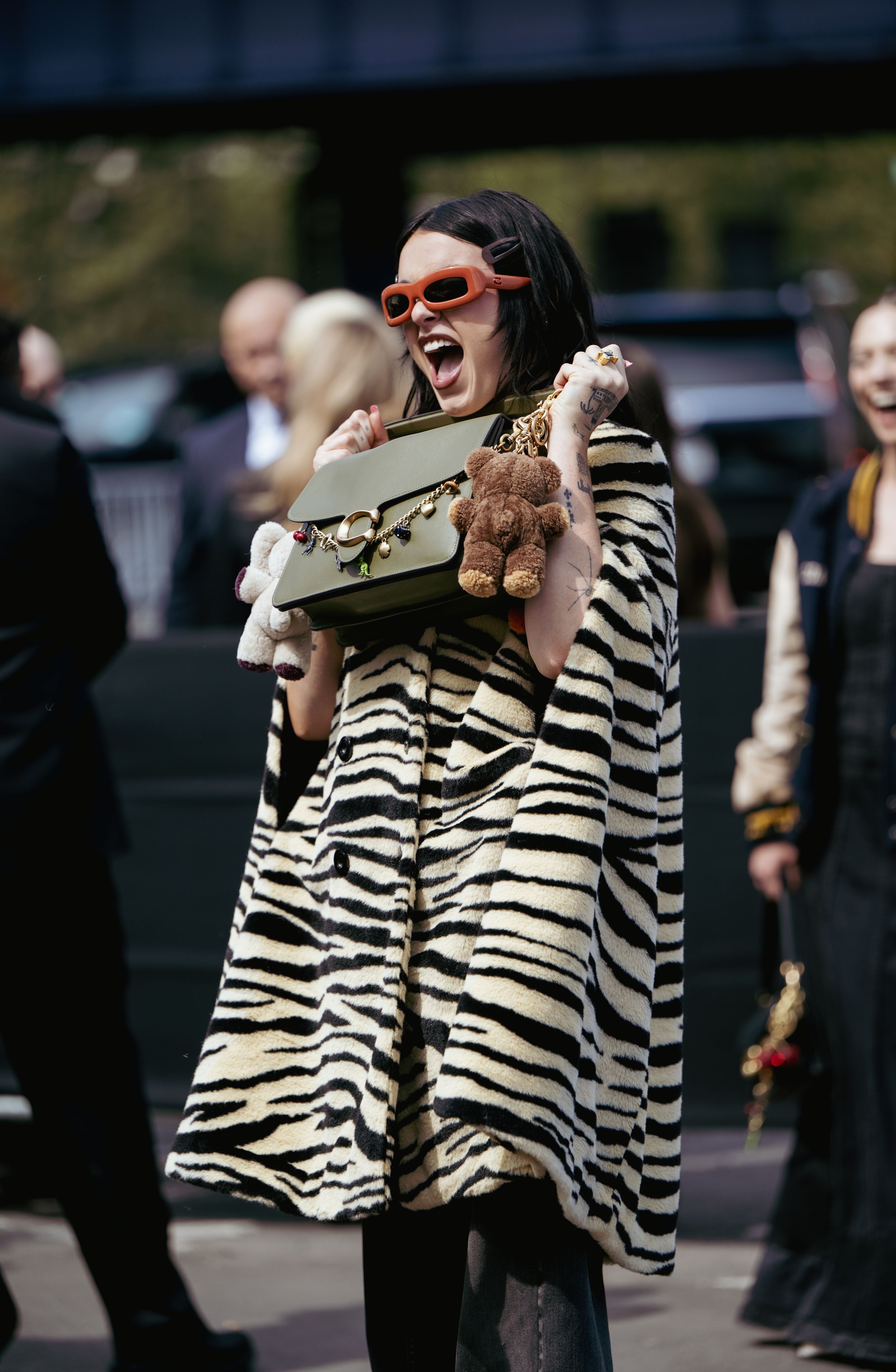 A person wearing a zebra print coat walks outdoors during a sunny day at a fashion event.