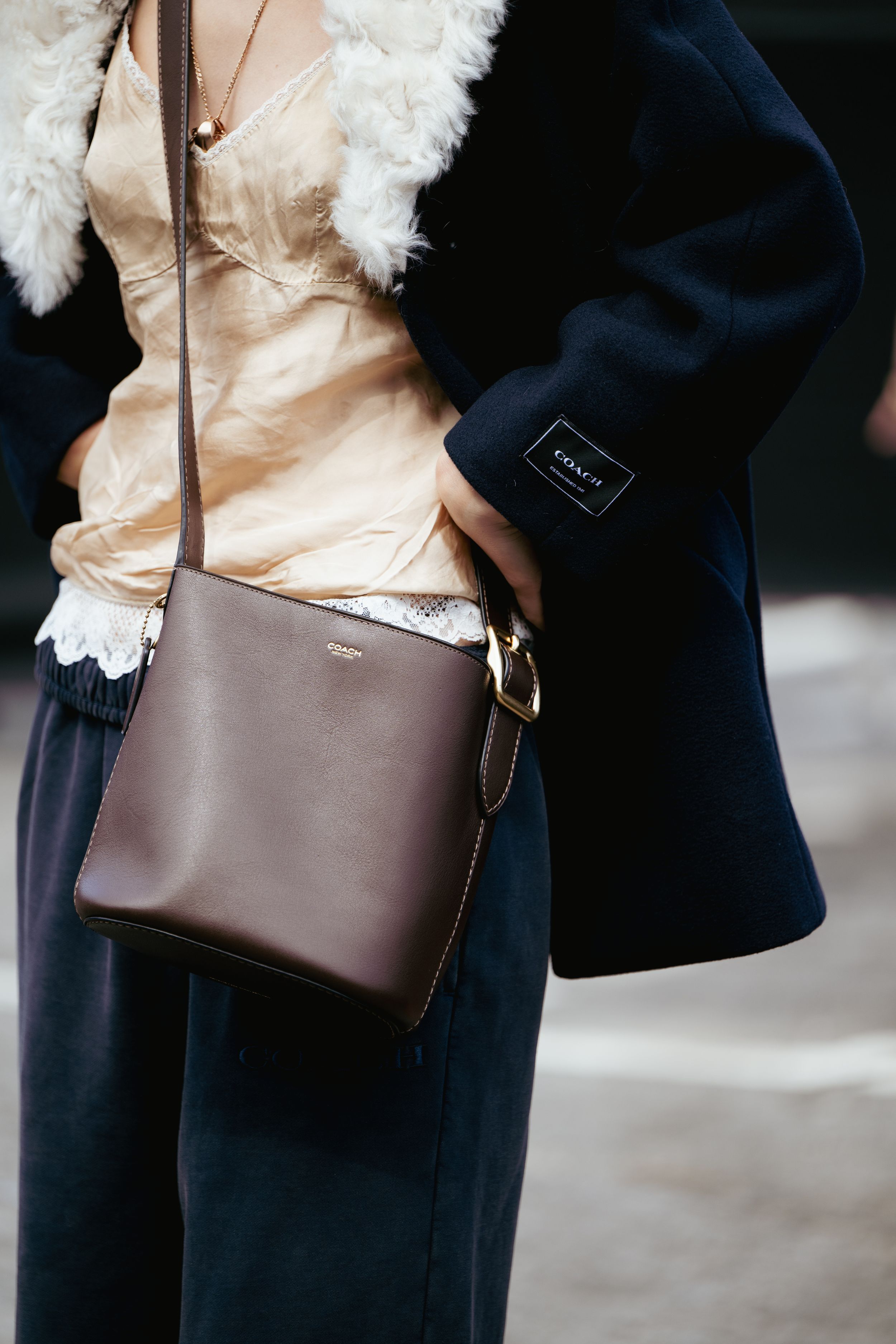A brown leather crossbody bag shown from multiple angles against a dark background with white fur trim visible.
