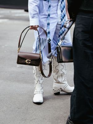 White studded combat boots with brown leather handbag and striped pants on city street.