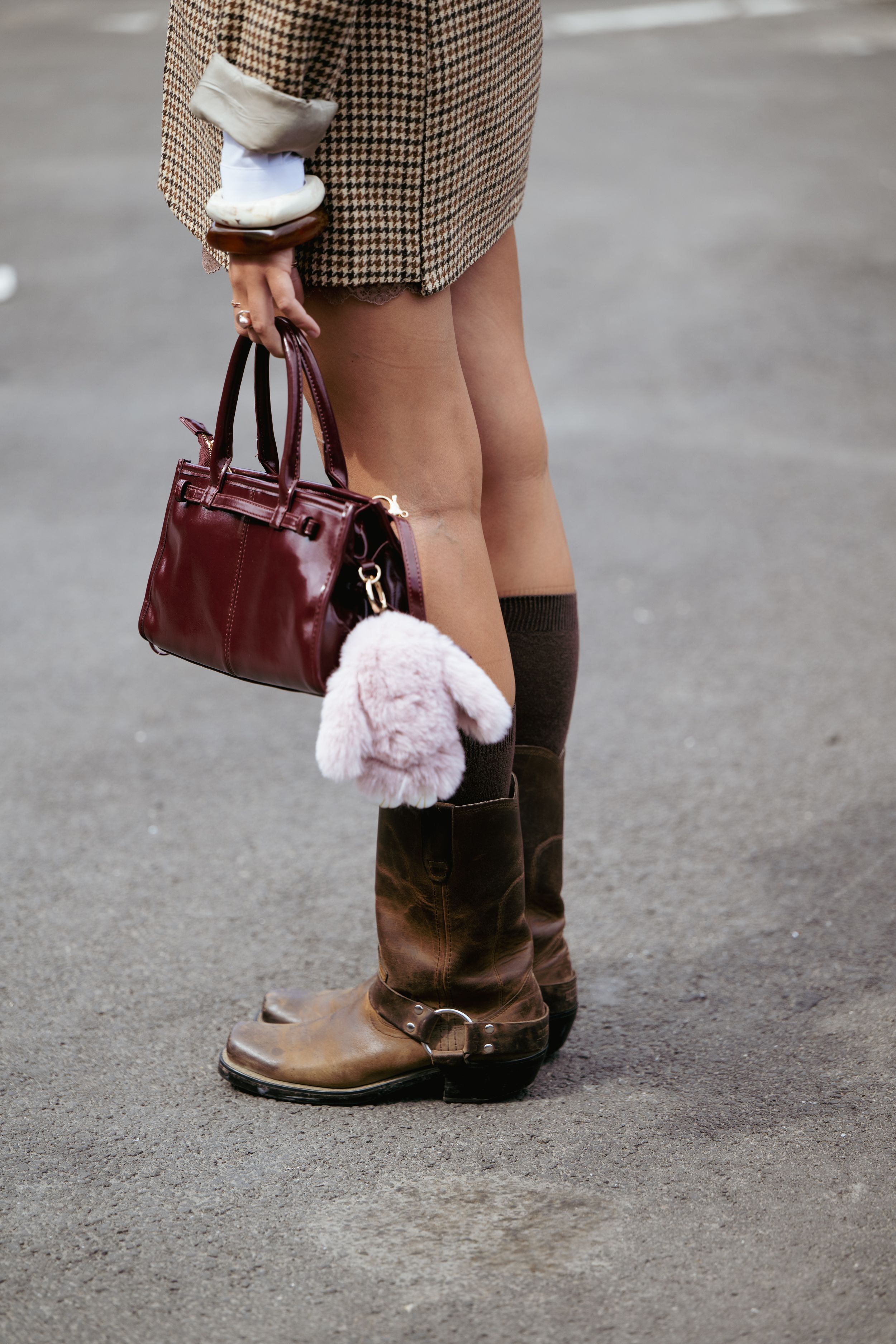Brown leather boots paired with black socks and a burgundy handbag on concrete ground.