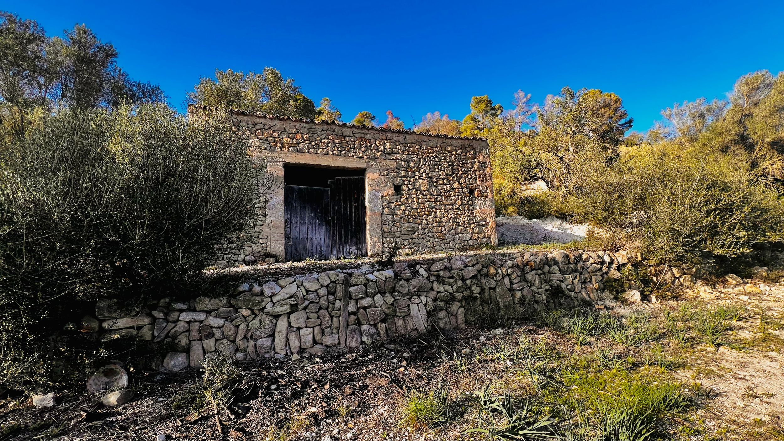 A panoramic view of stone ruins and ancient walls along a rocky hillside against a bright blue sky.