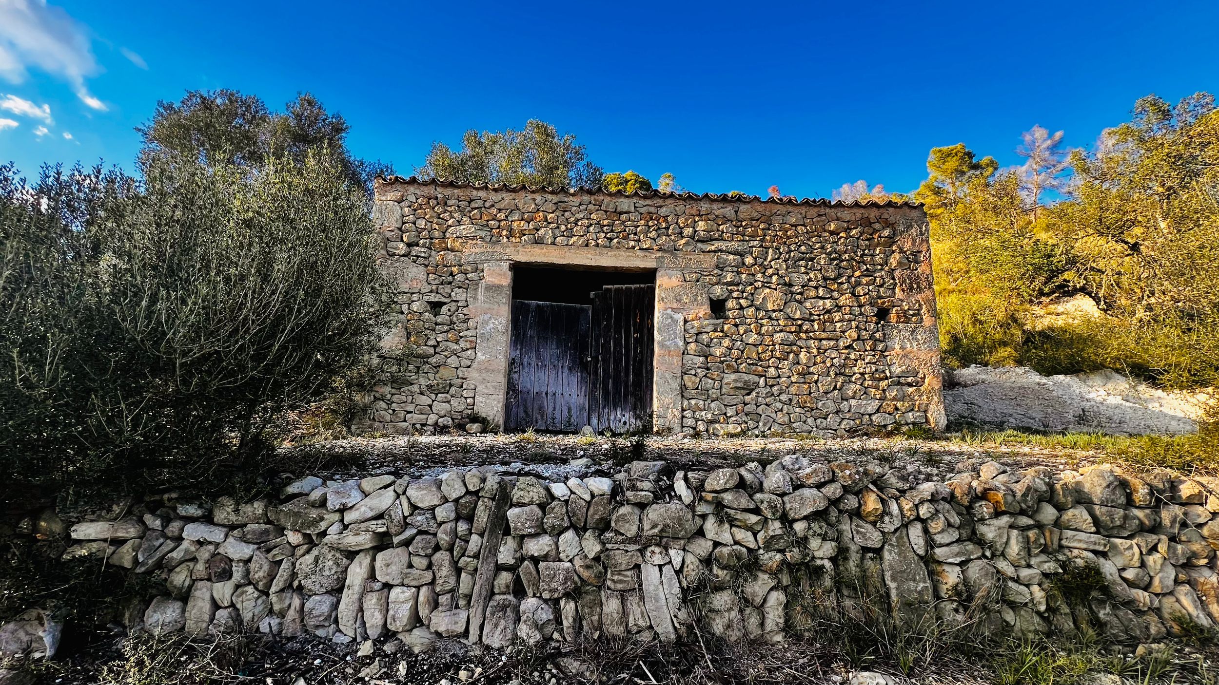 A panoramic view of ancient stone walls and ruins against a vibrant blue sky and autumn trees in the countryside.