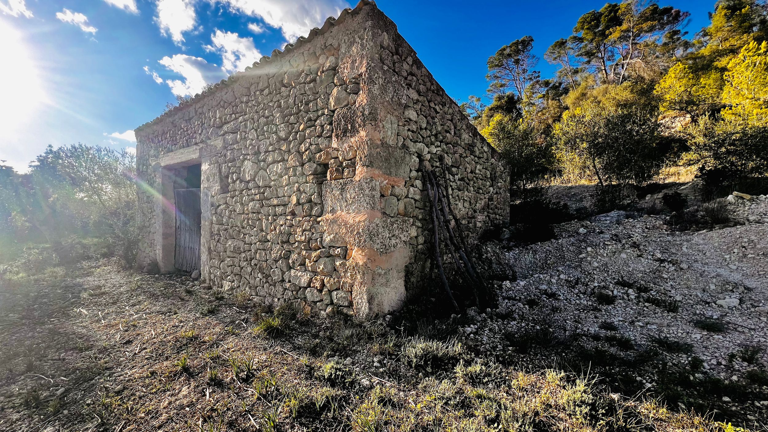 Ancient stone ruins of a castle wall stretch across a panoramic mountain landscape under bright blue skies.