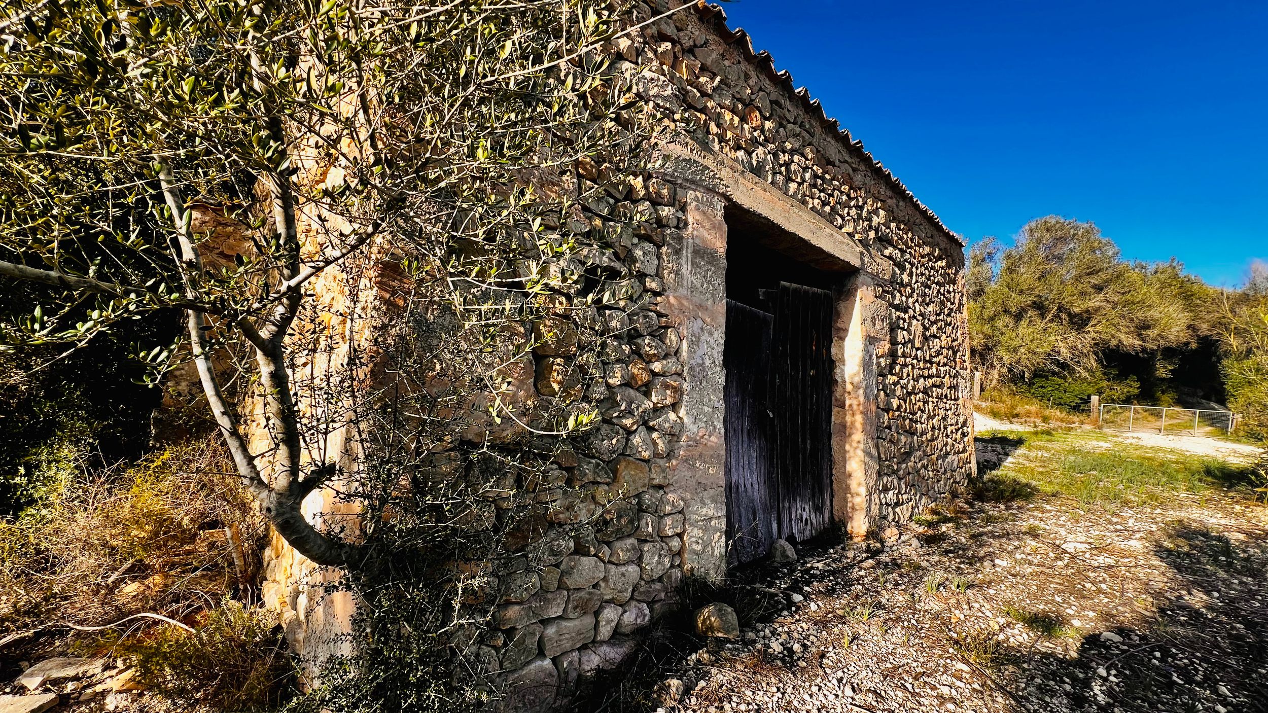 A panoramic view of an old stone building with multiple arched doorways against a bright blue sky.