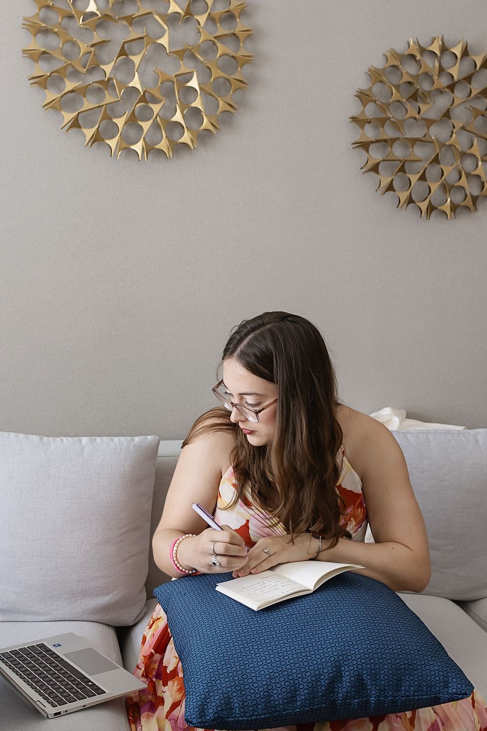 Person resting on a gray couch with decorative gold starburst wall art above and blue pillow.