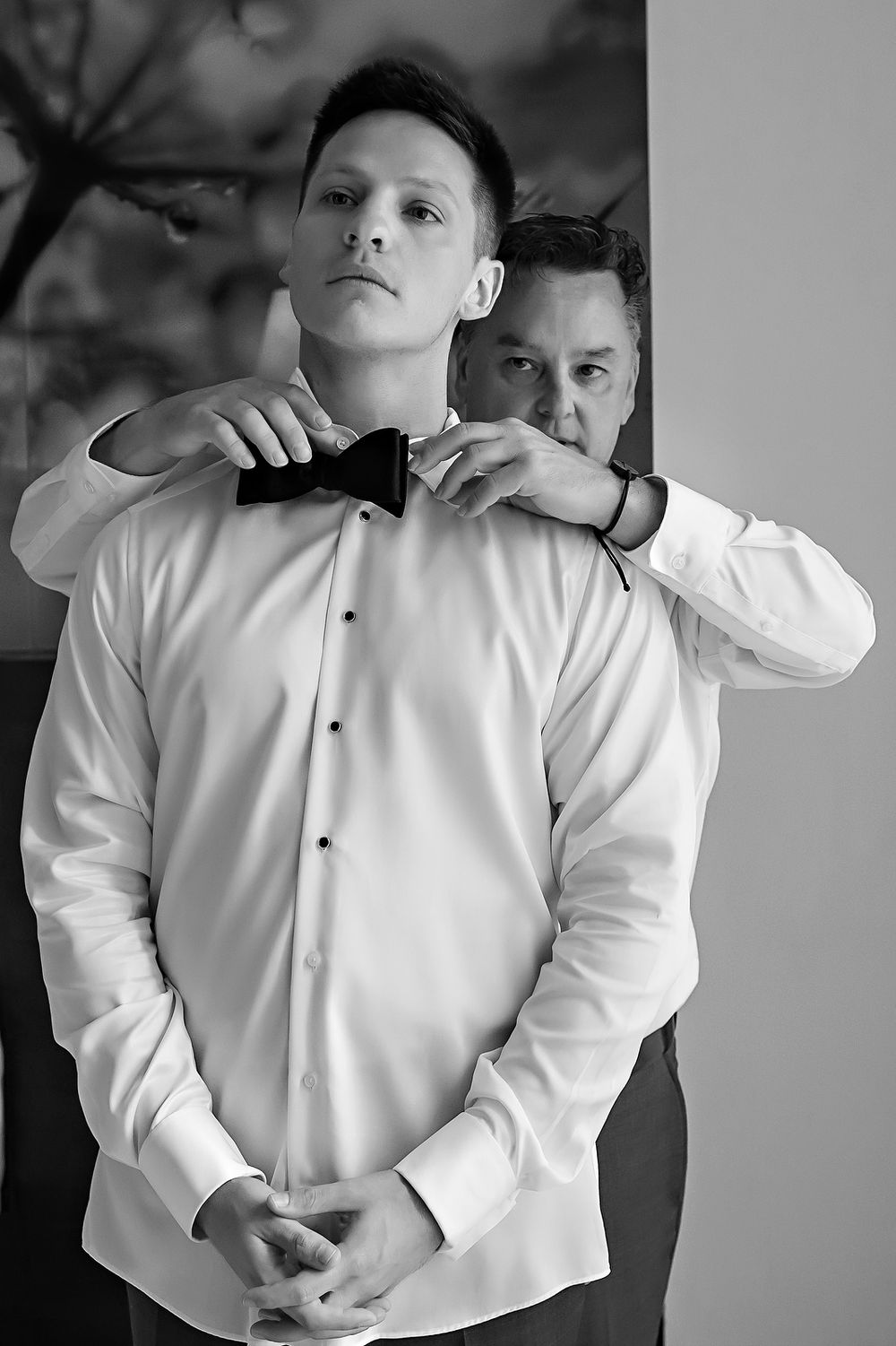 A black and white photo series showing someone adjusting the collar and buttons of a crisp white dress shirt.