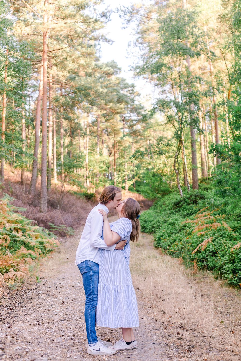 A romantic couple shares tender moments together while walking along a scenic forest path during golden hour.