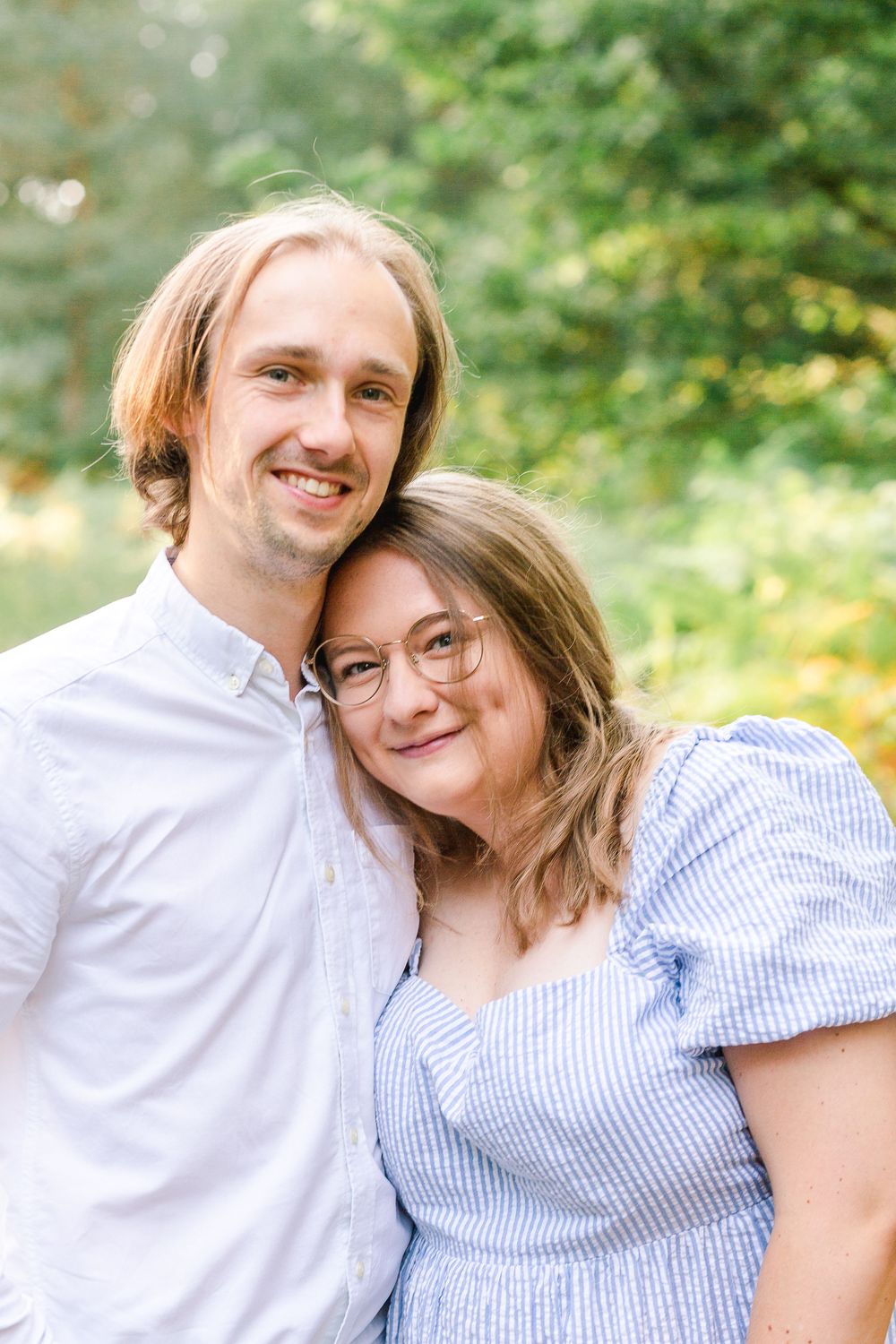 A couple in white and blue outfits smiling together outdoors with a blurred green background.